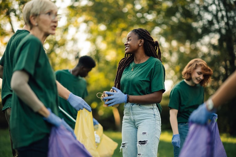 Group of diverse volunteers wearing green t-shirts and gloves collecting trash in park during community cleanup.