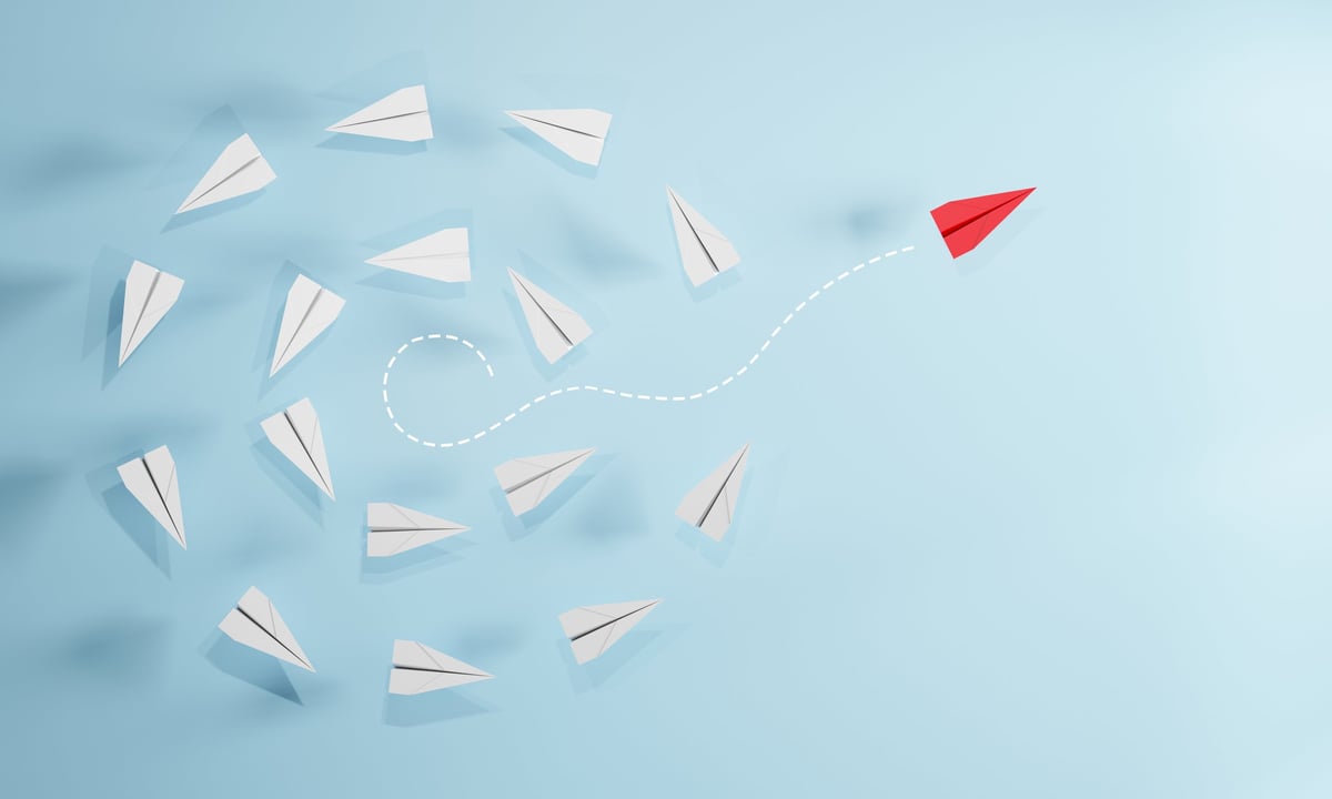 Red paper plane flying away from a group of white planes, representing individuality and a new direction