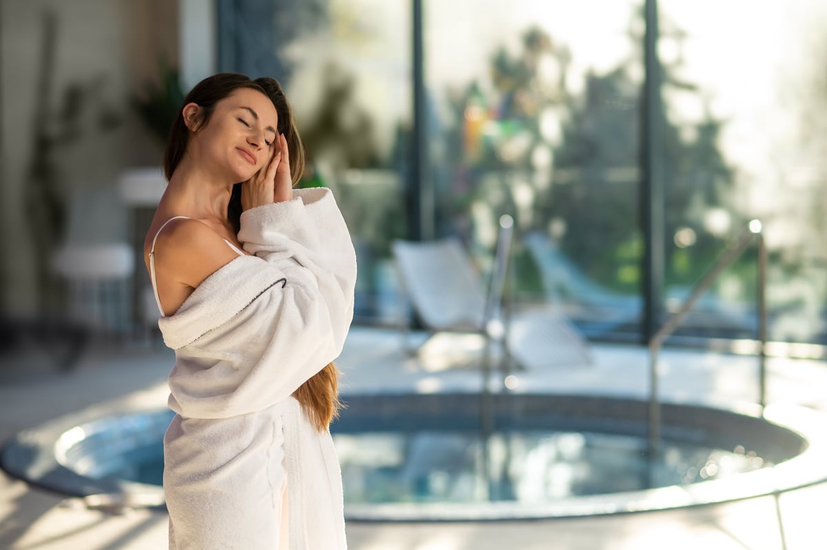 Relaxed woman in white bath robe standing near the pool in a spa center