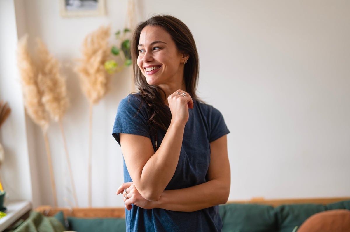 Happy young adult woman standing enjoying moment in casual clothing at home