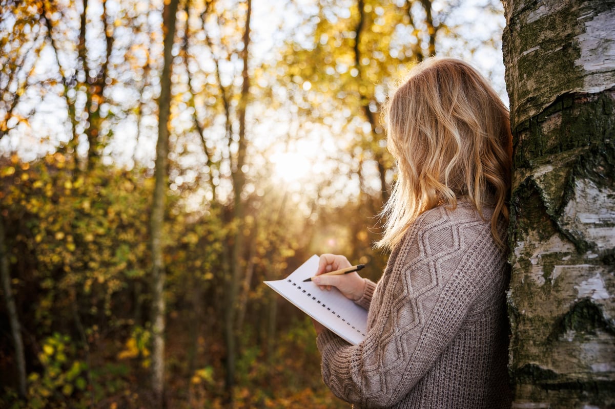Woman standing by birch tree writing in her diary. Peaceful moment in autumn forest and outdoor journaling