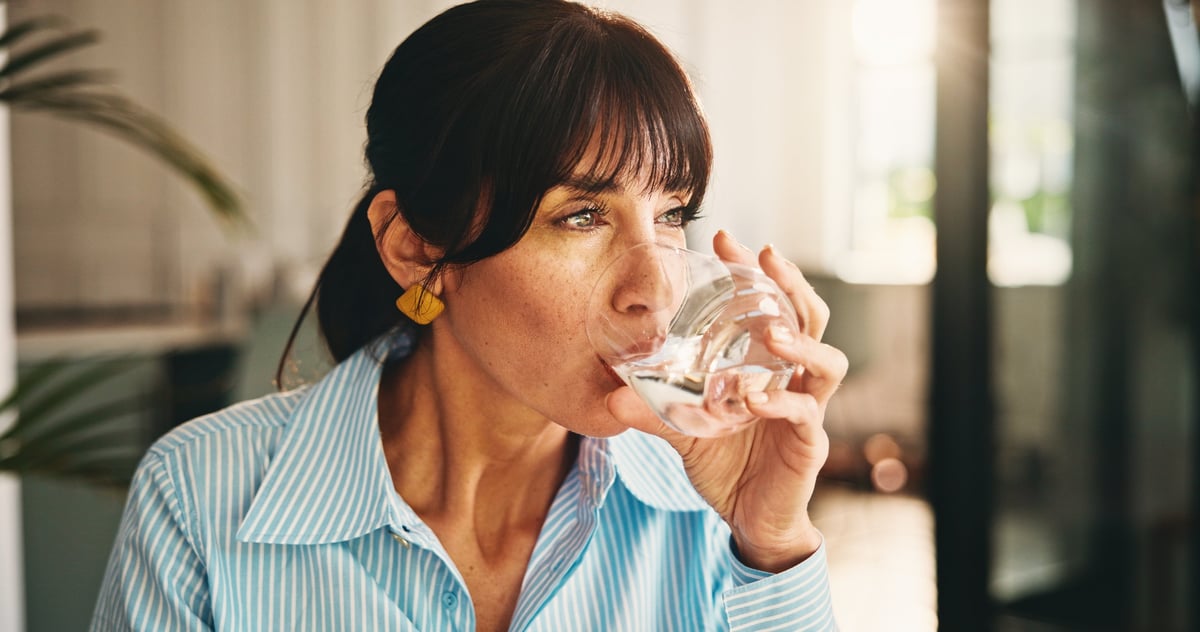 Home, woman and glass with water for wellness, hydration and benefits for gut health in living room. House, lounge and mature person with h2o drink for thirst, detox or nutrition in apartment