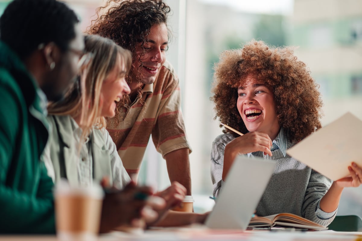 Group of diverse young adult students collaborating and laughing during a creative brainstorming session in a modern office
