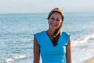 Woman wearing bright blue sleeveless top standing on sandy beach with ocean and waves in background