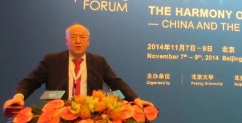 Man in dark suit speaking at podium with orange flowers, blue forum backdrop about China and Harmony, Beijing November 2014