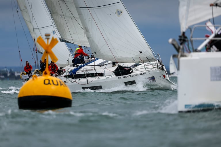 Sailboat racing in competition with crew members on deck, passing a yellow racing buoy marked OU in blue water