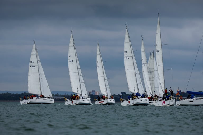 A fleet of white sailboats racing on blue water with overcast sky in the background