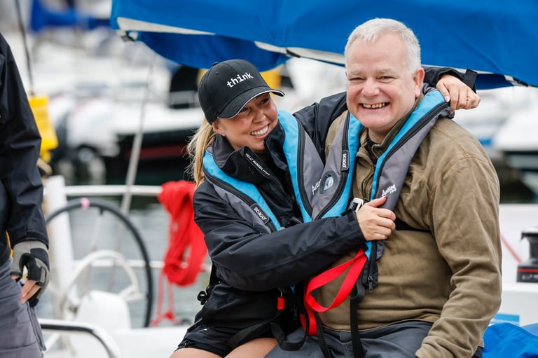 Two people wearing life jackets smile together on a boat with blue canopy and white boats visible in background