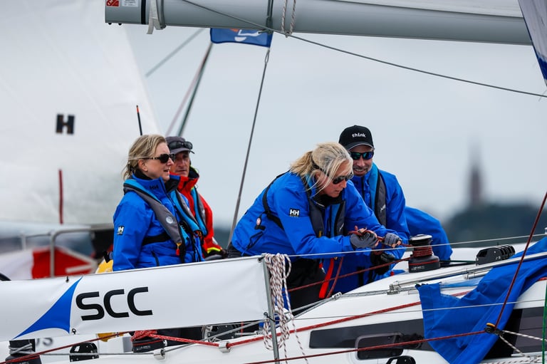 Four people in blue jackets on a sailboat deck working with ropes and equipment during sailing