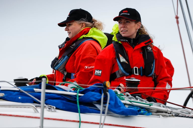 Two people in red and yellow safety gear on a sailboat, smiling while looking out at the water