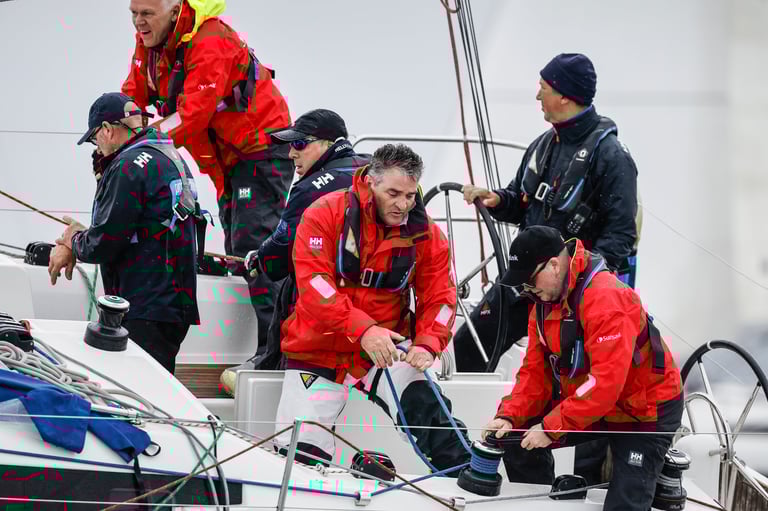 Professional sailing crew in red and black uniforms working on a yacht during a racing event