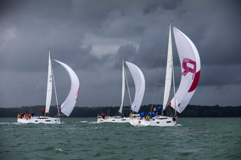 Three white sailboats racing on turquoise water under stormy gray skies