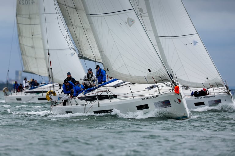 Two white sailboats racing on open water with crew members in blue shirts actively sailing