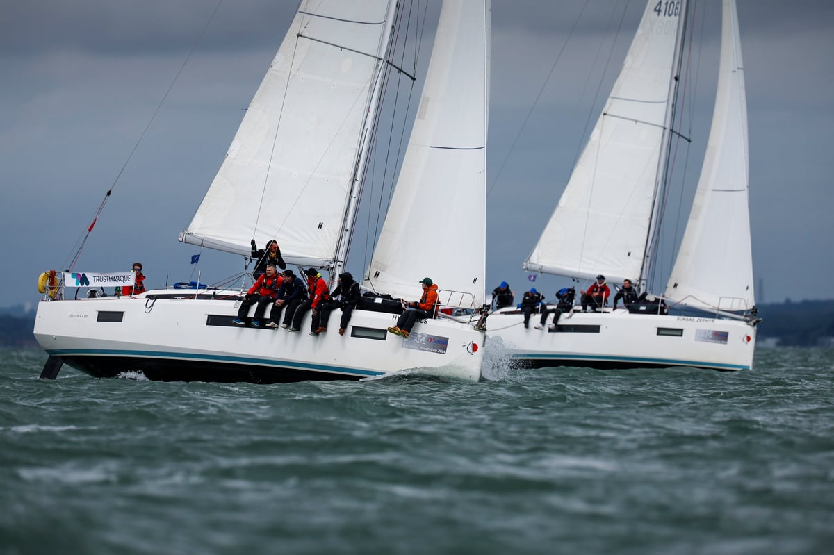 Two white sailboats with full sails racing on open water with crew members aboard