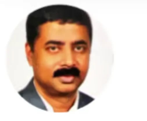 Professional headshot of a man with dark hair and mustache wearing a dark blazer against a light background