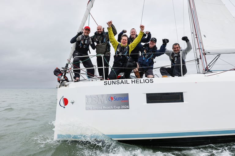 Group of people in wetsuits celebrating on a sailboat named Sunsail Helios in ocean waters