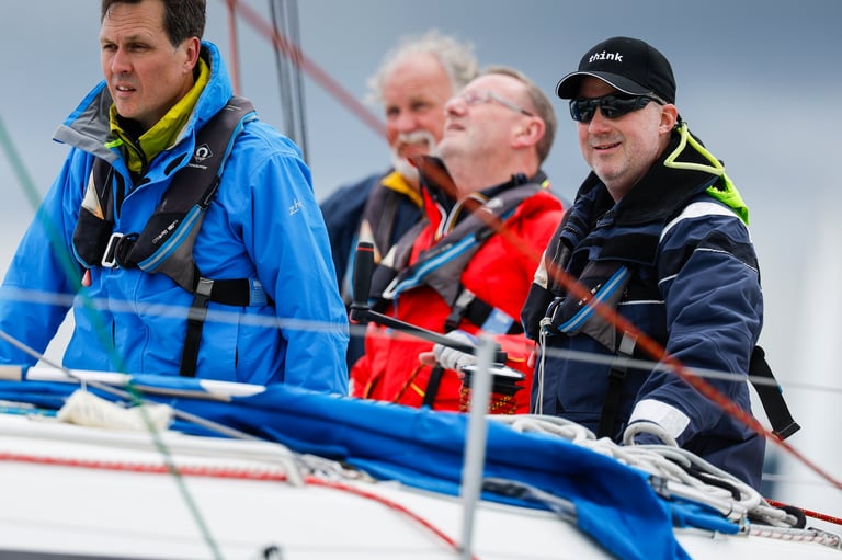 Four men in safety gear standing on a boat deck with rigging visible in the background