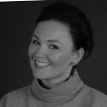 Black and white portrait of a smiling woman wearing a turtleneck against a dark background