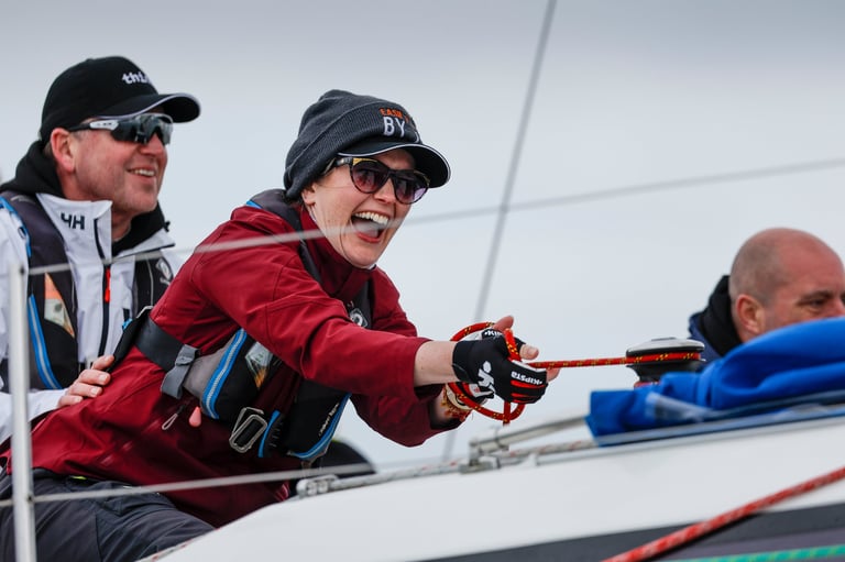 Three sailors on a boat deck handling red rope during a sailing activity, with one person in red jacket in the center